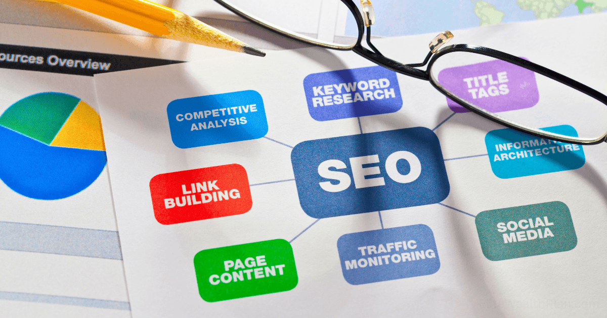 A paper with “SEO” in the center, surrounded by related terms like keyword research, SEO audit, title tags, social media, traffic monitoring, page content, and link building. Glasses and a pencil lie nearby.
