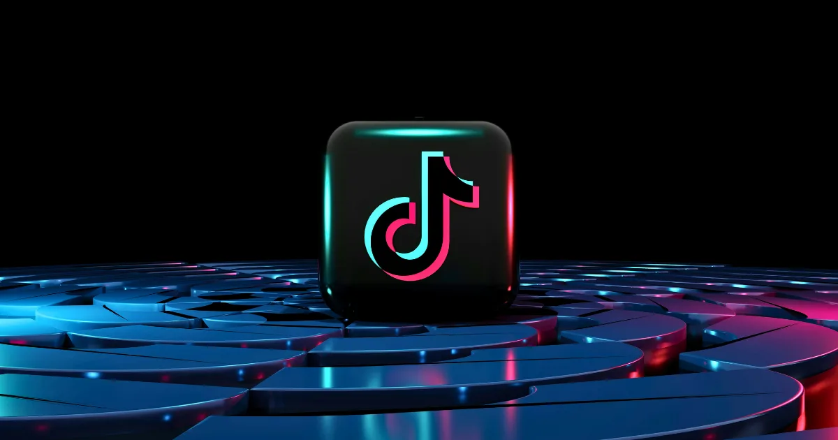 A black cube featuring the TikTok logo stands on a reflective, circular blue and pink platform with glowing accents, symbolizing the power of TikTok algorithm hacks against a dark background.