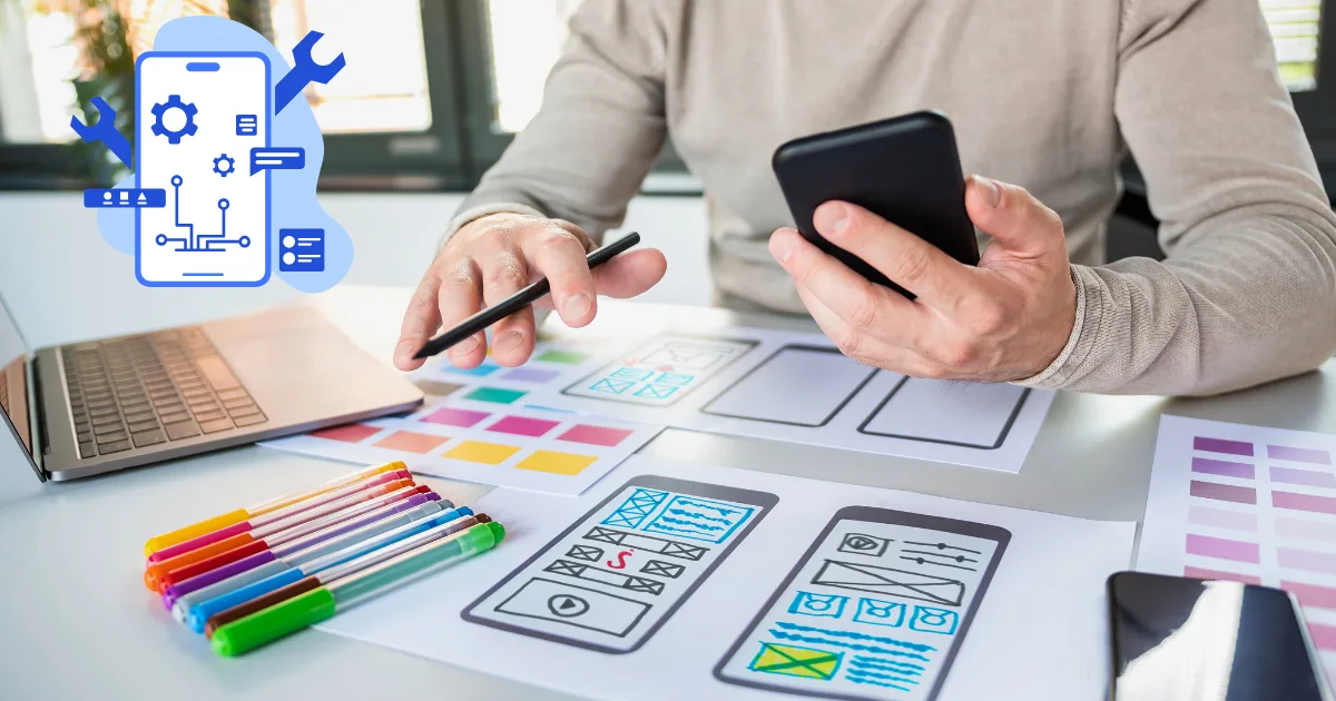 A person holds a smartphone and a pen, working on mobile app design sketches at a desk with colored markers—a scene capturing the start of an app development journey. A graphic of a phone with technical icons is overlaid on the image.