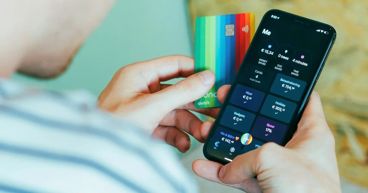 A person holds a colorful debit card in one hand and a smartphone in the other, displaying a business banking setup with account balances and transactions on the screen.