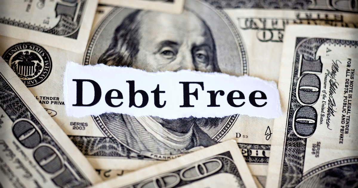A torn piece of paper with the words Debt Free is placed over several scattered U.S. one hundred dollar bills, symbolizing a successful debt elimination strategy.