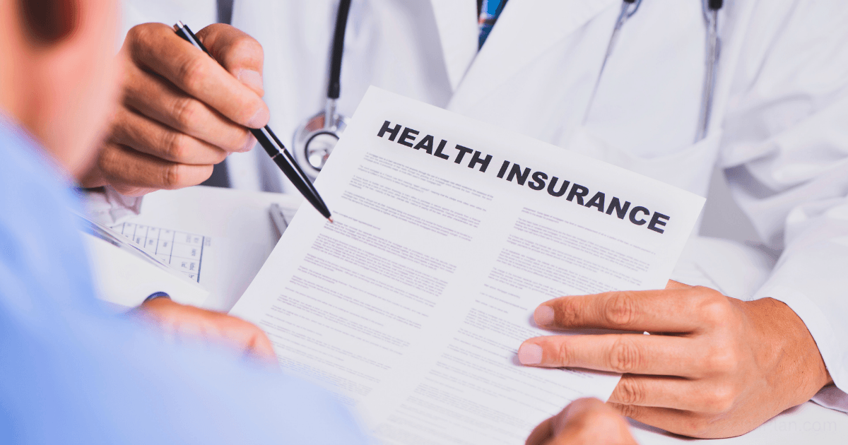 A doctor in a white coat explains a health insurance for entrepreneurs document to a patient, pointing at the paperwork with a pen during a consultation.