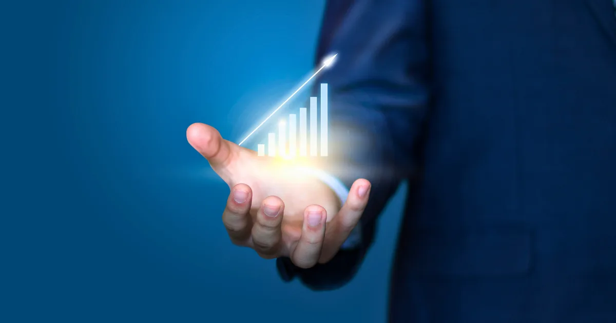 A person in a suit holds out their hand, with a glowing holographic bar graph and upward arrow floating above the palm, symbolizing investment portfolio growth and financial success.