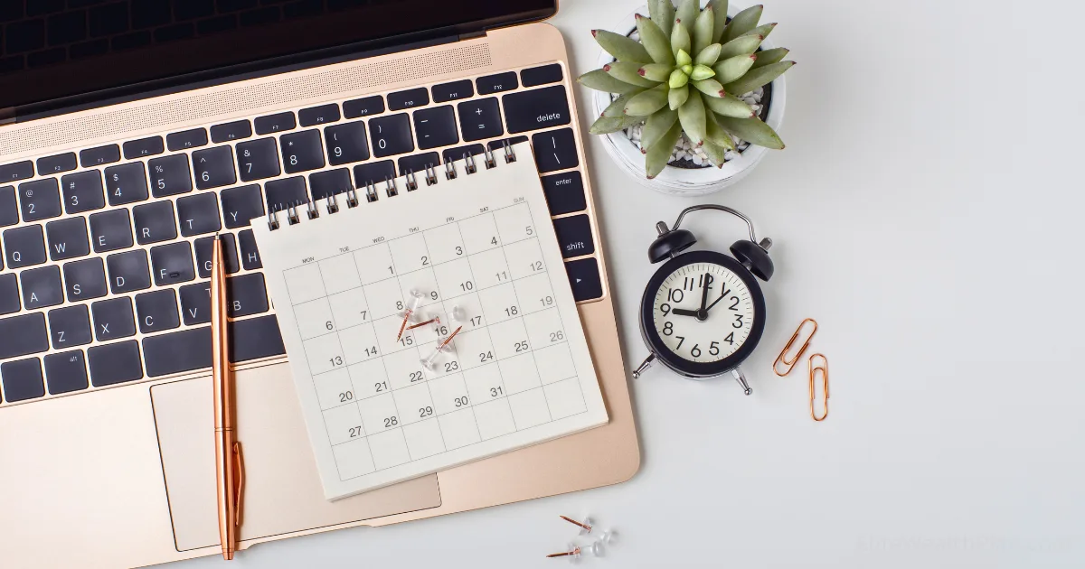 A perfect content calendar, pen, black alarm clock, gold paper clips, and a small potted succulent are arranged on a laptop keyboard on a white desk.