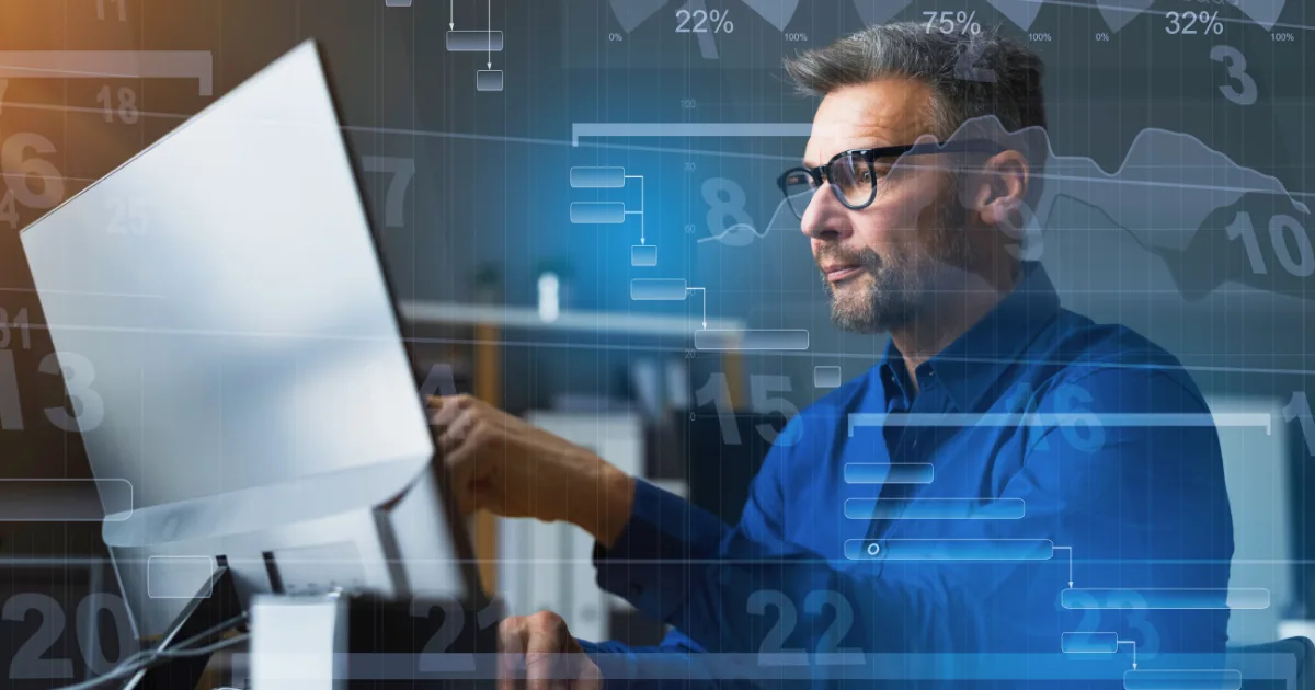 A man wearing glasses works at a computer in an office. Overlaid graphics of charts, graphs, and numbers suggest data analysis or financial work, possibly using project management tools. The blurred background highlights a focused work environment.