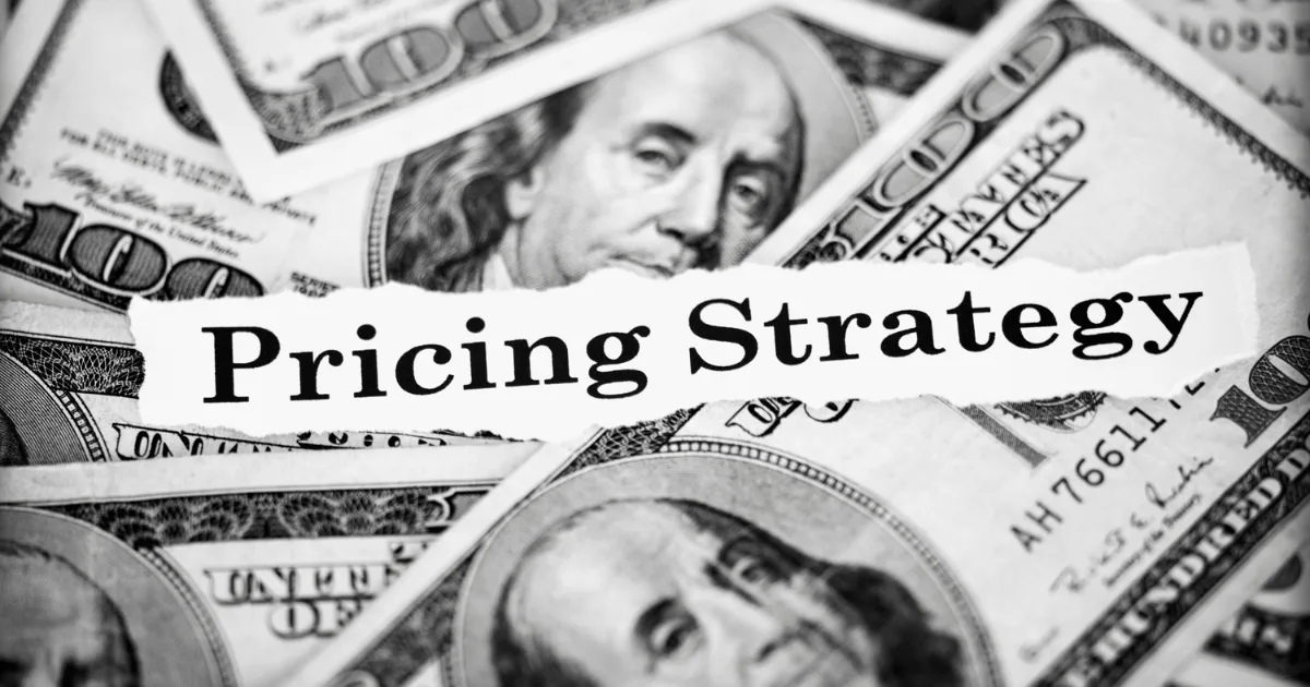 A torn piece of paper with the words “Pricing Strategy” sits atop scattered U.S. one hundred dollar bills, hinting at the influence of psychological pricing on revenue decisions.