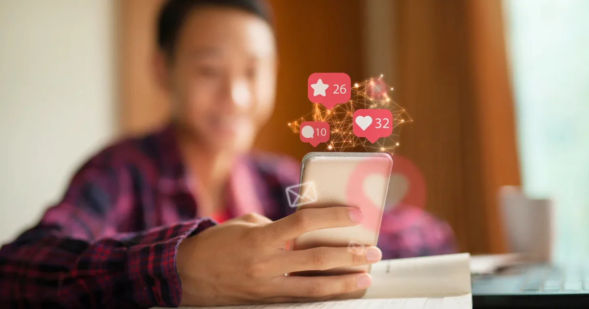A person holding a smartphone smiles while looking at the screen, as notification icons for likes, comments, and messages appear above the phone—capturing a true social media success story.