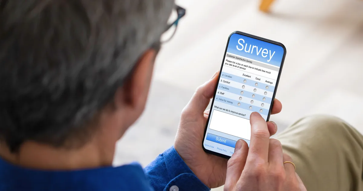 A person holding a smartphone is filling out an online survey on one of the top survey websites, selecting responses from multiple-choice options on the screen with their finger.