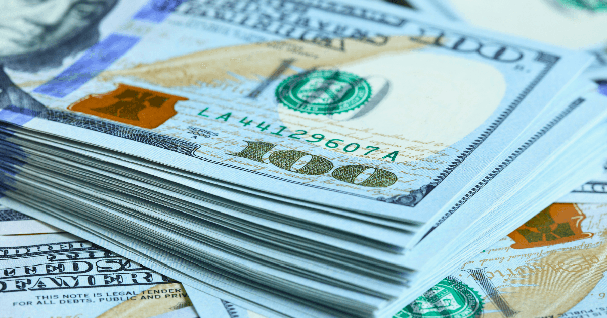 A close-up of a stack of U.S. one hundred dollar bills, often featured in an income report, shows the number 100 in gold, a green Treasury seal, and part of Benjamin Franklin’s portrait.